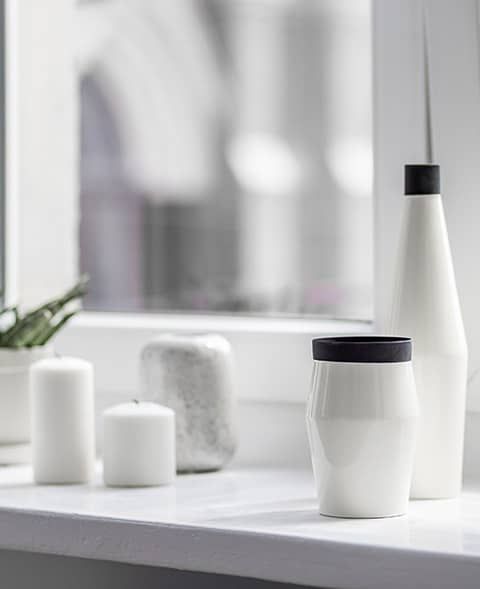 Mehrere weiße Behälter und Kerzen auf Natursteinfensterbank